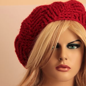 May include: A woman with long blonde hair is wearing a red knitted beret. The beret has a simple, classic design.