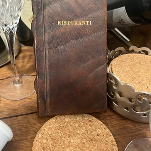 May include: A brown leather-bound book with the word "RISTCRANTI" embossed in gold lettering on the front cover.