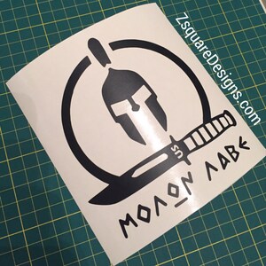 May include: Black and white vinyl decal featuring a Spartan helmet inside a circle, a knife, and the text "MOLON LABE".