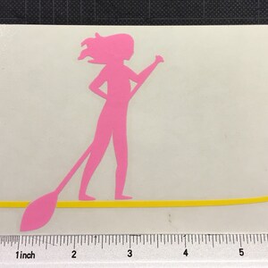 May include: Pink silhouette of a person paddleboarding on a yellow surfboard. The person is holding a paddle in their right hand.