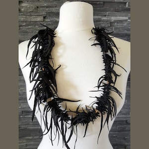 May include: A black leather necklace with a fringe design. The necklace is made of many small pieces of leather that are woven together to create a unique and textured look.
