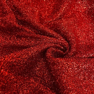 May include: Red sparkly fabric with a textured surface. The fabric is wrinkled and folded.
