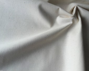 May include: A close-up of a piece of off-white fabric with a slightly textured surface. The fabric is folded and draped, showing its soft and natural texture.