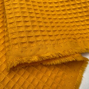 Puede incluir: Un tejido de punto de waffle amarillo con un borde deshilachado.