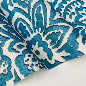 May include: Close-up of a white fabric with a teal blue floral pattern. The fabric is folded and the pattern is visible on both sides.