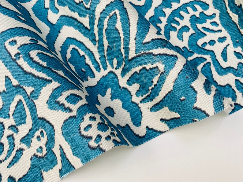May include: Close-up of a white fabric with a teal blue floral pattern. The fabric is folded and the pattern is visible on both sides.
