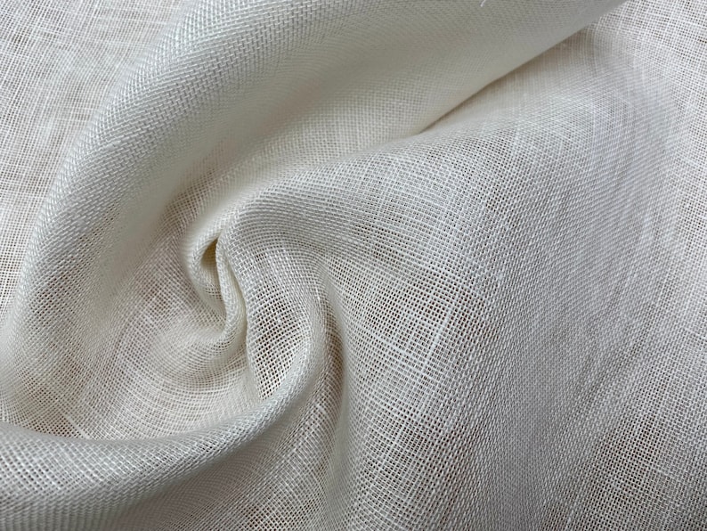 May include: Close-up of a white linen fabric with a woven texture. The fabric is folded and draped, showing its soft and natural texture.