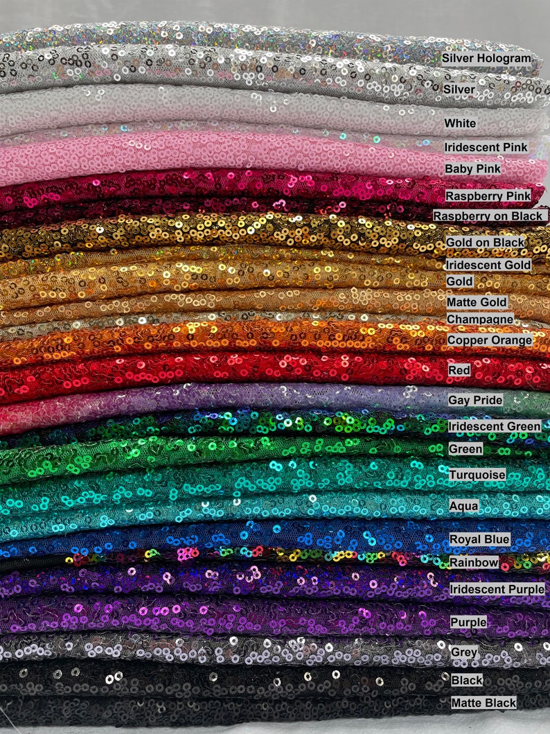 Pode incluir: Uma pilha de tecidos de lantejoulas em uma variedade de cores, incluindo prata, branco, rosa, vermelho, ouro, verde, azul e roxo. Cada tecido &eacute; rotulado com o nome da sua cor, como "Silver Hologram", "Baby Pink" e "Royal Blue".