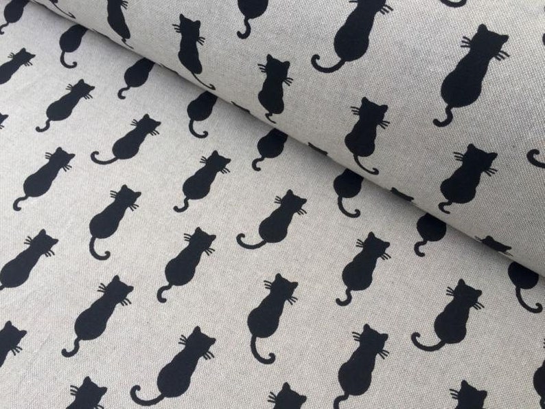 Puede incluir: Una tela beige con un patr&oacute;n repetido de siluetas de gatos negros. Los gatos est&aacute;n mirando hacia la derecha y est&aacute;n en varias posiciones.