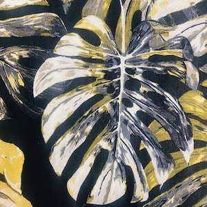 May include: A black fabric with a large white and yellow leaf pattern. The leaf has a detailed vein pattern and is reminiscent of a monstera plant.