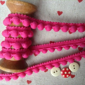 May include: Pink pom-pom trim on a wooden spool with three buttons, one with white dots on a red background.