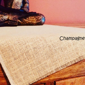 May include: A beige burlap table runner with a fringed edge. The text "Champagne" is printed on the runner.