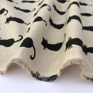 Puede incluir: Una tela beige con un patr&oacute;n de silueta de gato negro. La tela tiene un borde sin terminar y est&aacute; doblada.