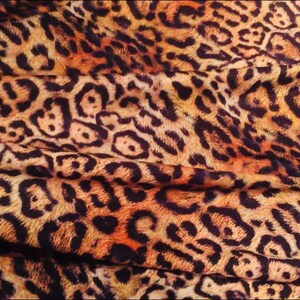K&ouml;nnte beinhalten: Nahaufnahme eines Stoffes mit Leopardenmuster. Der Stoff ist braun, orange und schwarz mit einer weichen, flauschigen Textur.