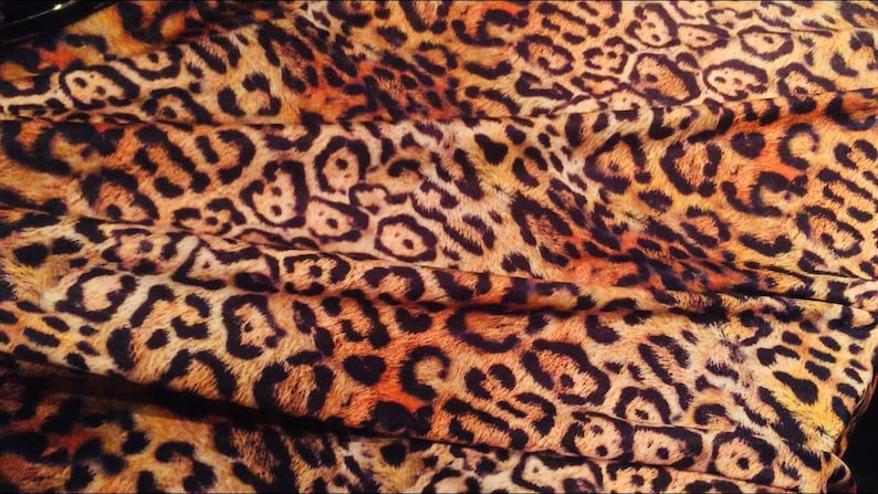 K&ouml;nnte beinhalten: Nahaufnahme eines Stoffes mit Leopardenmuster. Der Stoff ist braun, orange und schwarz mit einer weichen, flauschigen Textur.