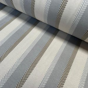 May include: Close-up of a fabric roll with a repeating striped pattern. The stripes alternate between light gray, medium gray, and off-white. Each stripe features a herringbone design in a darker gray color.