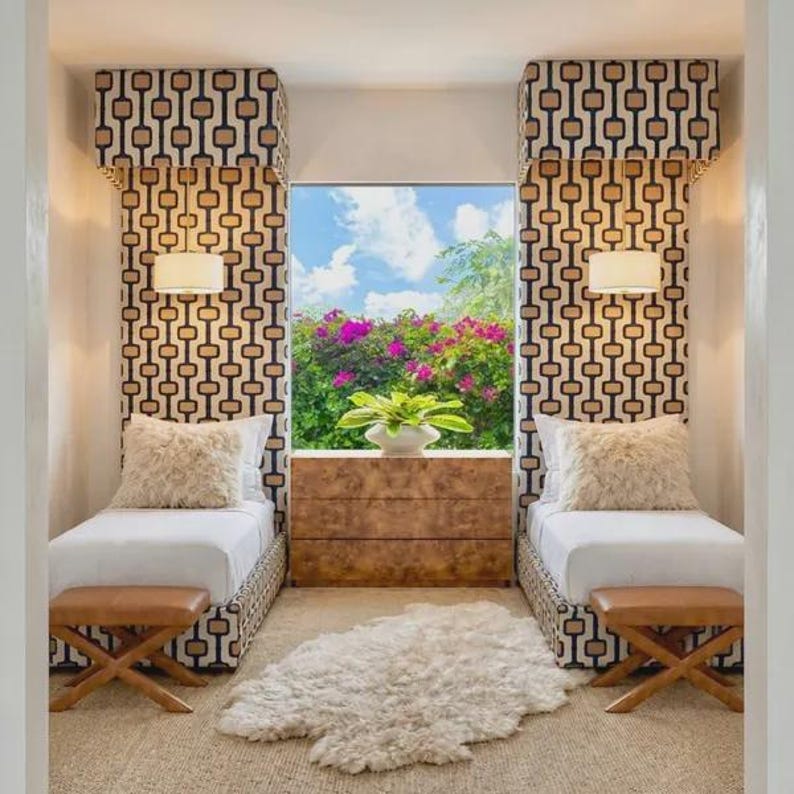 May include: Two twin beds with white bedding and fluffy cream pillows are positioned on either side of a wooden dresser. Above each bed is a tall, patterned fabric headboard with a hanging white pendant light. A white faux fur rug sits on the floor.