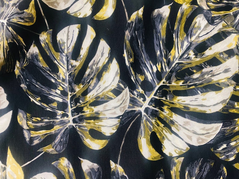 May include: Black fabric with a large-scale print of gold and gray tropical leaves.