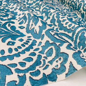 May include: Teal and white fabric with a repeating floral pattern. The fabric has a textured surface.