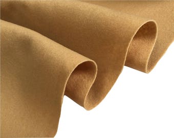 May include: Close-up of a folded piece of tan felt fabric. The fabric has a soft, textured appearance with visible fibers. The folds create shadows and depth, highlighting the material's thickness and drape. The color is a warm, neutral tone.