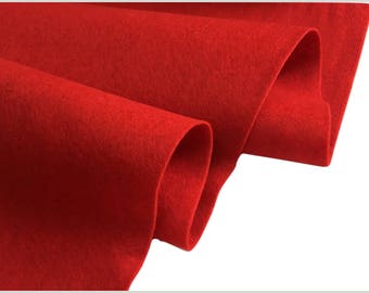 May include: Close-up of a vibrant red felt fabric, folded and draped. The material has a soft, textured appearance, with visible fibers. The folds create shadows and depth, highlighting the fabric's thickness and color. The background is white.