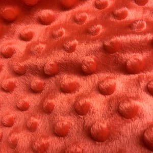 May include: Close-up of a red fabric with a textured, raised dot pattern. The fabric has a soft, plush feel.