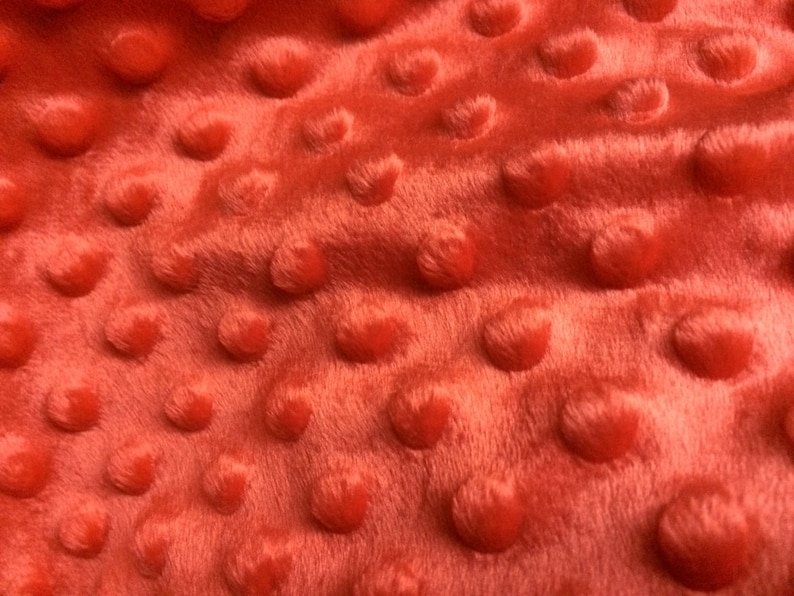 May include: Close-up of a red fabric with a textured, raised dot pattern. The fabric has a soft, plush feel.