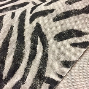Peut inclure: Gros plan sur un tissu beige avec un imprim&eacute; z&egrave;bre noir. Le tissu a une apparence textur&eacute;e et tiss&eacute;e.