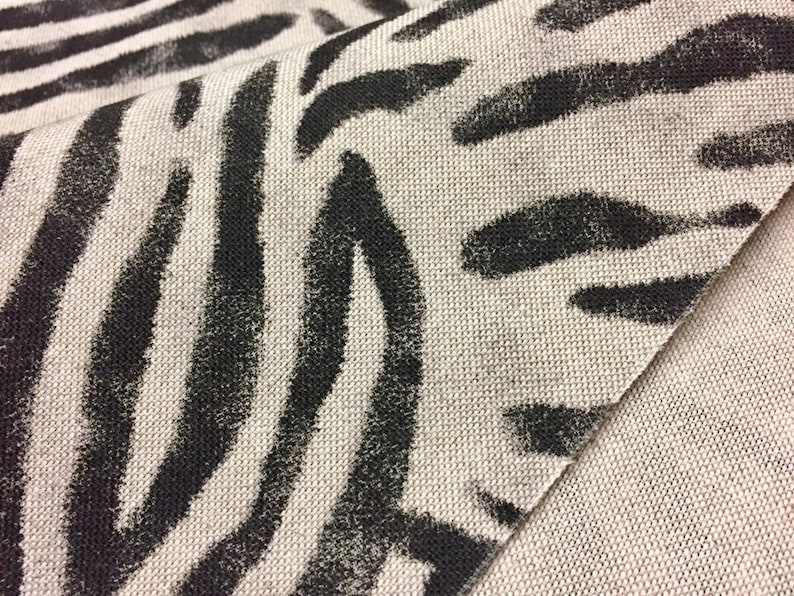 Peut inclure: Gros plan sur un tissu beige avec un imprim&eacute; z&egrave;bre noir. Le tissu a une apparence textur&eacute;e et tiss&eacute;e.