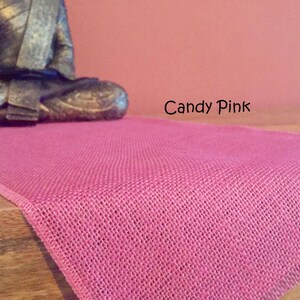 May include: A pink burlap table runner with a subtle woven texture. The runner is on a wooden surface and the text "Candy Pink" is visible in the image.