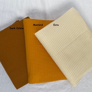 Puede incluir: Tres muestras de tejido de tejido de waffle en ocre oscuro, amarillo mostaza y crudo.