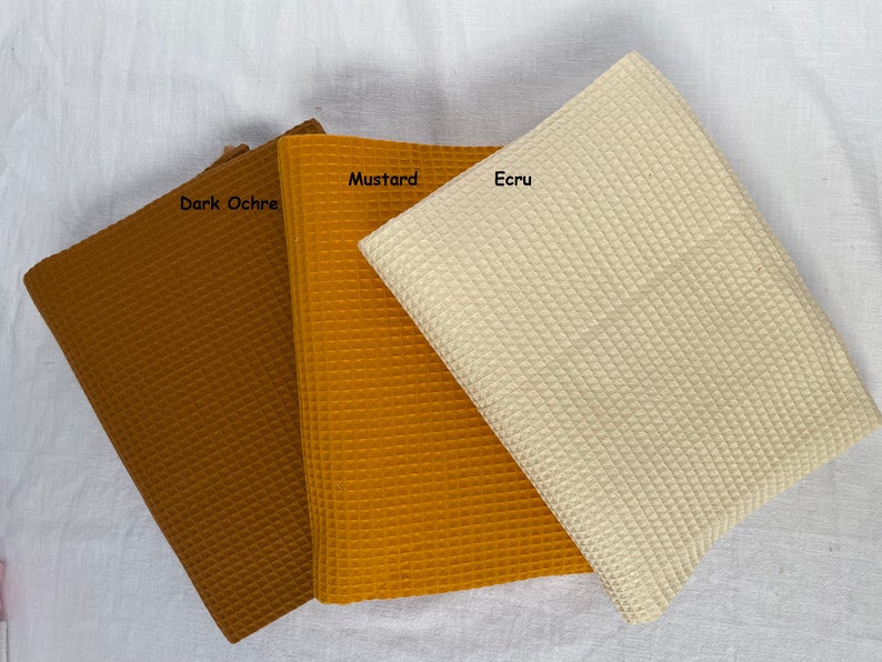 Puede incluir: Tres muestras de tejido de tejido de waffle en ocre oscuro, amarillo mostaza y crudo.