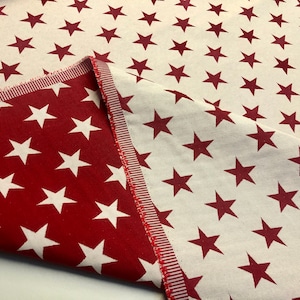 May include: Red fabric with a white star pattern. The fabric is folded over to show the reverse side, which has a white background with a red star pattern.