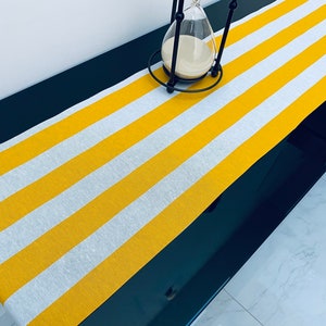 May include: Yellow and white striped table runner on a black table. The table runner is made of fabric and has a subtle sheen.