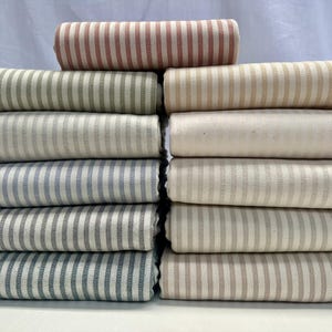 May include: Rolled fabric rolls in a variety of colours, including red, green, blue, and grey, all featuring vertical striped patterns. The fabrics are neatly stacked, showcasing a range of textile options.