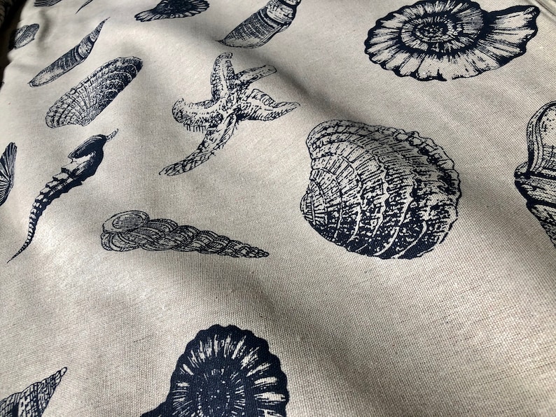 May include: A beige fabric with a repeating pattern of black and white sea life illustrations. The pattern includes starfish, seashells, and seahorses.