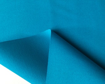 May include: A close-up of a teal blue fabric with a smooth, even texture. The fabric is folded in half, creating a sharp crease.