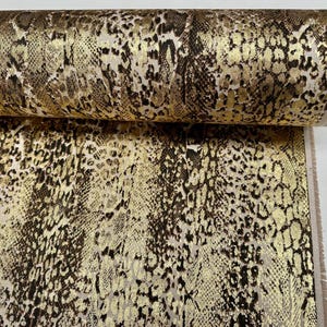 May include: Close-up of a fabric with a gold and brown snake skin pattern.