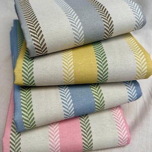 May include: A stack of folded fabric with vertical stripes in various colors. The stripes include light blue, gray, yellow, green, and pink, with a white background. Each stripe has a herringbone pattern in a contrasting color.