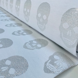 Op de afbeelding: Witte stof met een herhalend patroon van zilveren glitter schedelontwerpen.