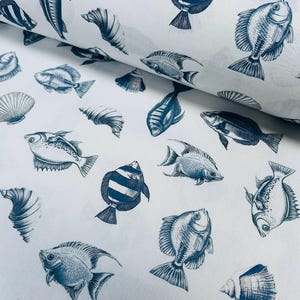 May include: White fabric with a repeating pattern of blue fish and seashells. The fish vary in shape and size, with detailed illustrations. The seashells are also depicted in a detailed, artistic style. The fabric is likely for crafting or home decor.
