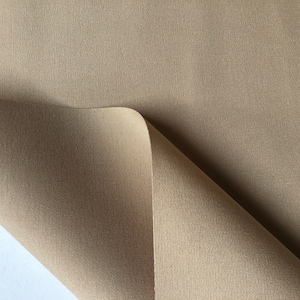 Può includere: Primo piano di un tessuto marrone con una texture sottile. Il tessuto è piegato, rivelando un lato inferiore marrone più chiaro.