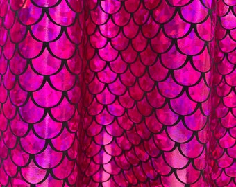 May include: Close-up of a pink iridescent fabric with a mermaid scale pattern. The scales are outlined in black and have a holographic finish.