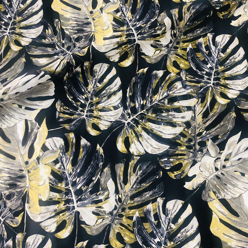 May include: Black fabric with a repeating pattern of large, gold and gray tropical leaves.