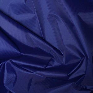 May include: A close-up of a deep blue fabric with a subtle, textured pattern. The fabric is folded and draped, creating shadows and highlights that emphasize its texture and sheen. The overall appearance suggests a high-quality material.