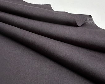 Puede incluir: Primer plano de una tela gris oscuro con una textura sutil. La tela está doblada y drapeada, mostrando su aspecto suave y liso.