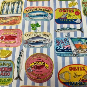 Può includere: Un tessuto con un motivo ripetuto di colorate scatole di sardine e sgombri, insieme a pesci e fette di limone, su uno sfondo a righe blu e bianche. Le scatole presentano vari marchi e design.