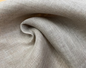 May include: A close-up of a light brown linen fabric with a textured weave. The fabric is folded and draped, showing its soft and natural texture.