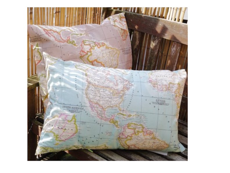 May include: Two decorative throw pillows with a world map print. The top pillow is pink with a light blue map, and the bottom pillow is light blue with a darker blue map.