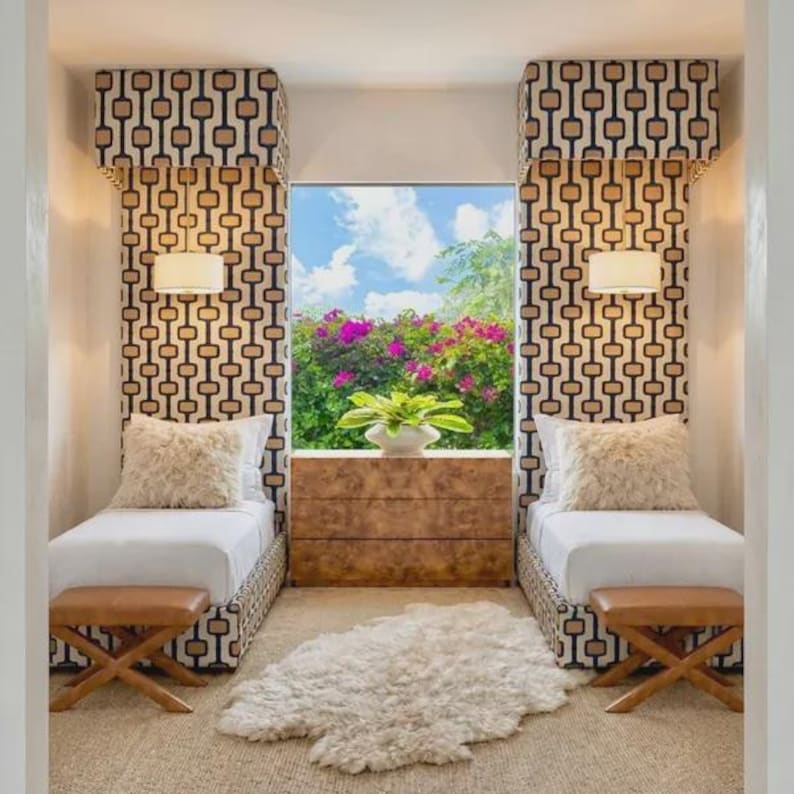 Op de afbeelding: Twee eenpersoonsbedden met wit beddengoed en pluizige cr&egrave;mekleurige kussens staan aan weerszijden van een houten dressoir. Boven elk bed hangt een hoog, gestoffeerd hoofdeinde met een witte hanglamp. Een wit imitatiebont kleed ligt op de vloer.
